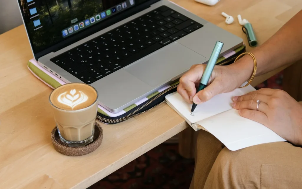 Notebook, laptop, and coffee on a desk